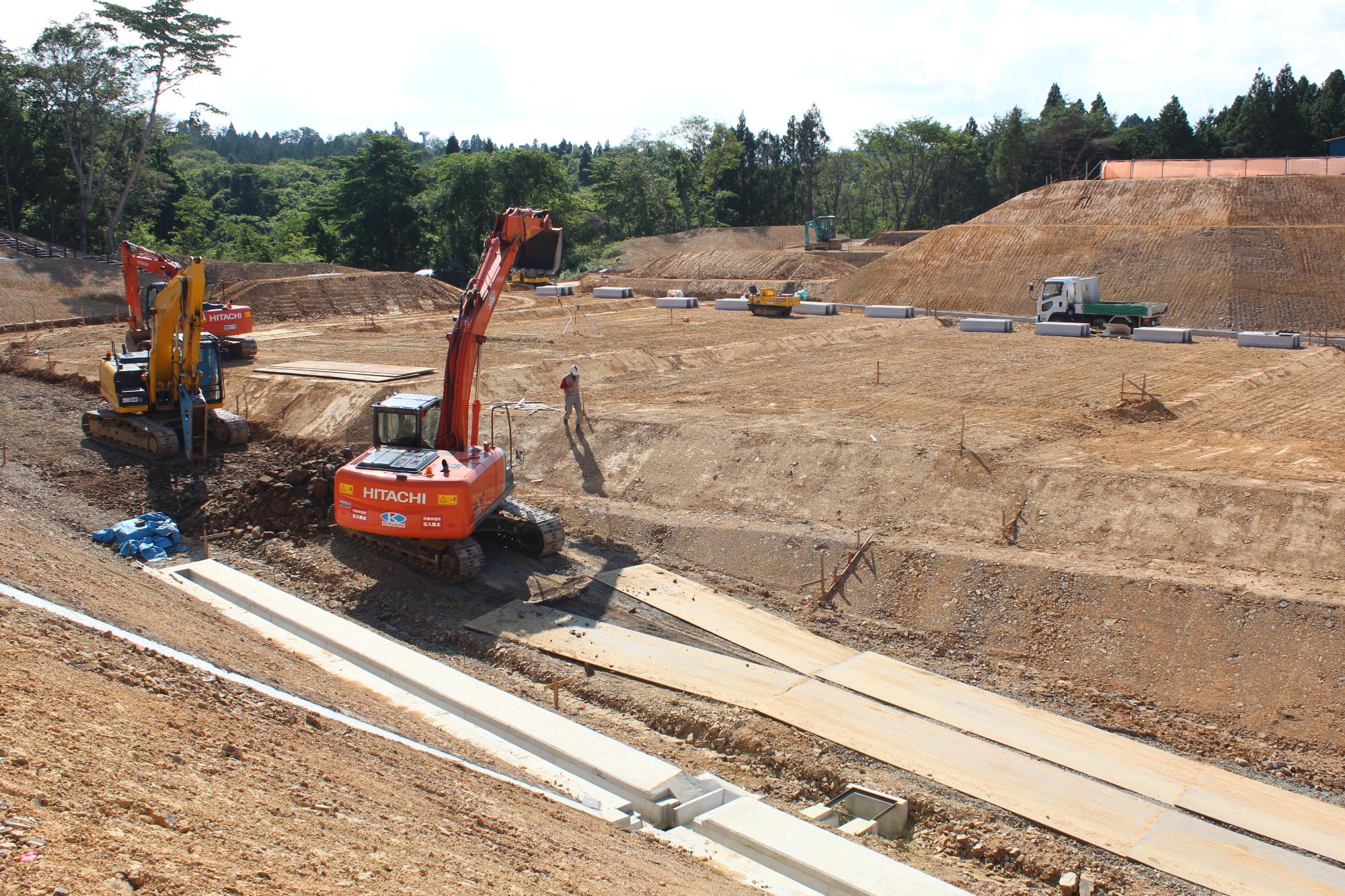 重機や作業員が、傾斜地にコンクリートの水路を設置する工事を進めている様子を写した写真
