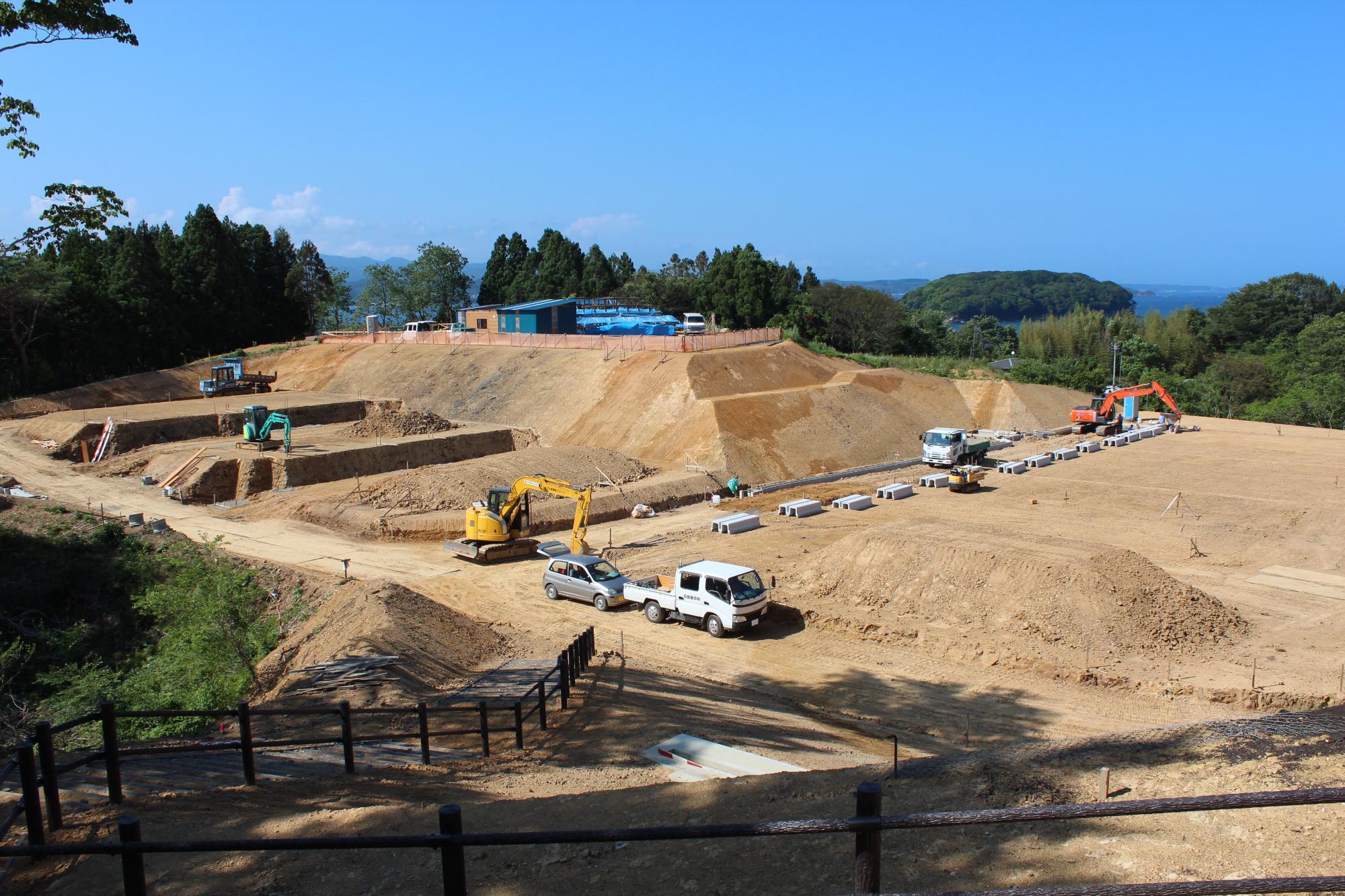 山あいの広い敷地で重機や車両が稼働し、段々畑のように造成工事が進められている様子を写した写真