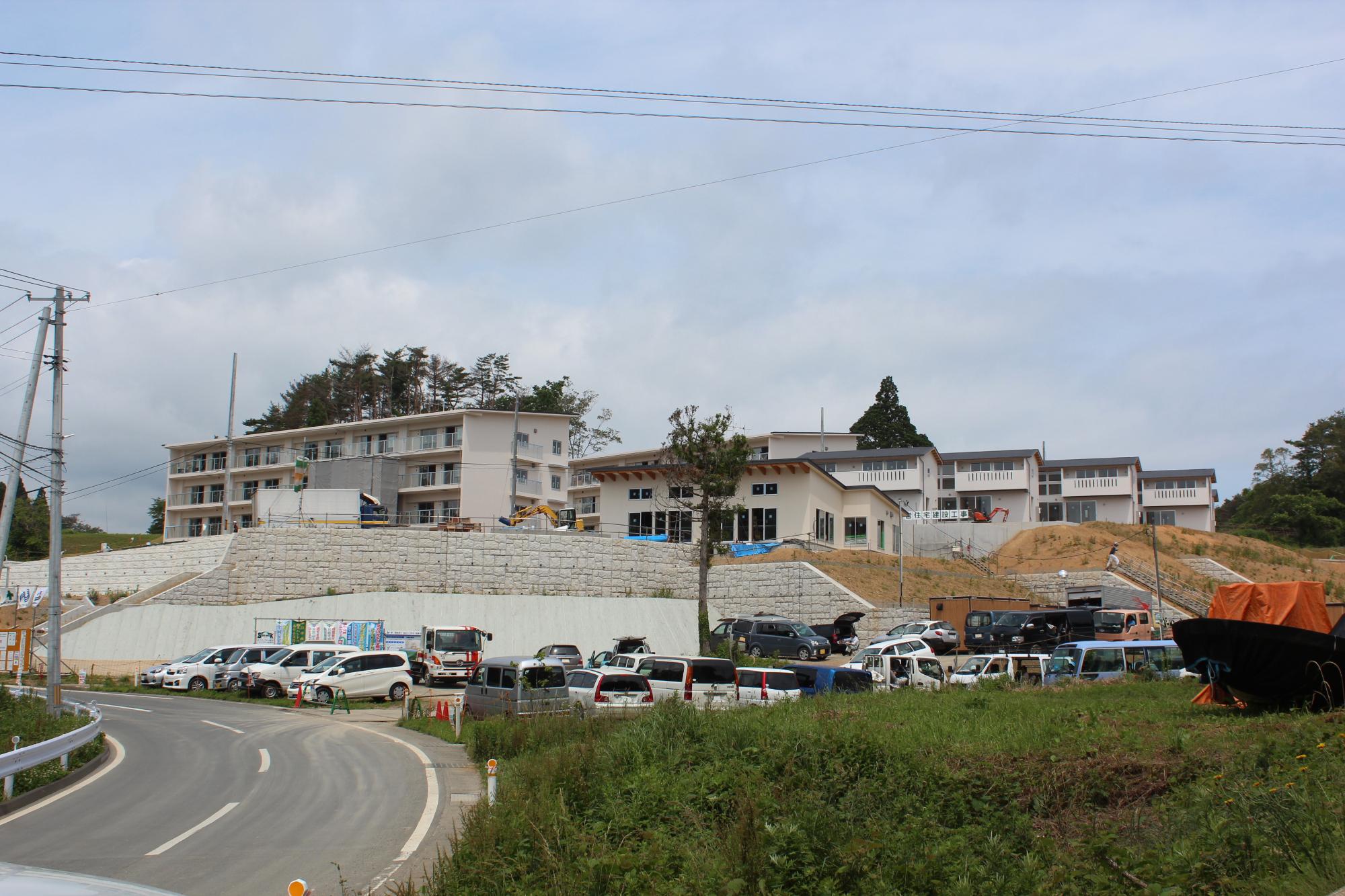 工事が完了して複数の住宅棟が完成し、駐車場には車が並ぶ高台の災害公営住宅全景の写真