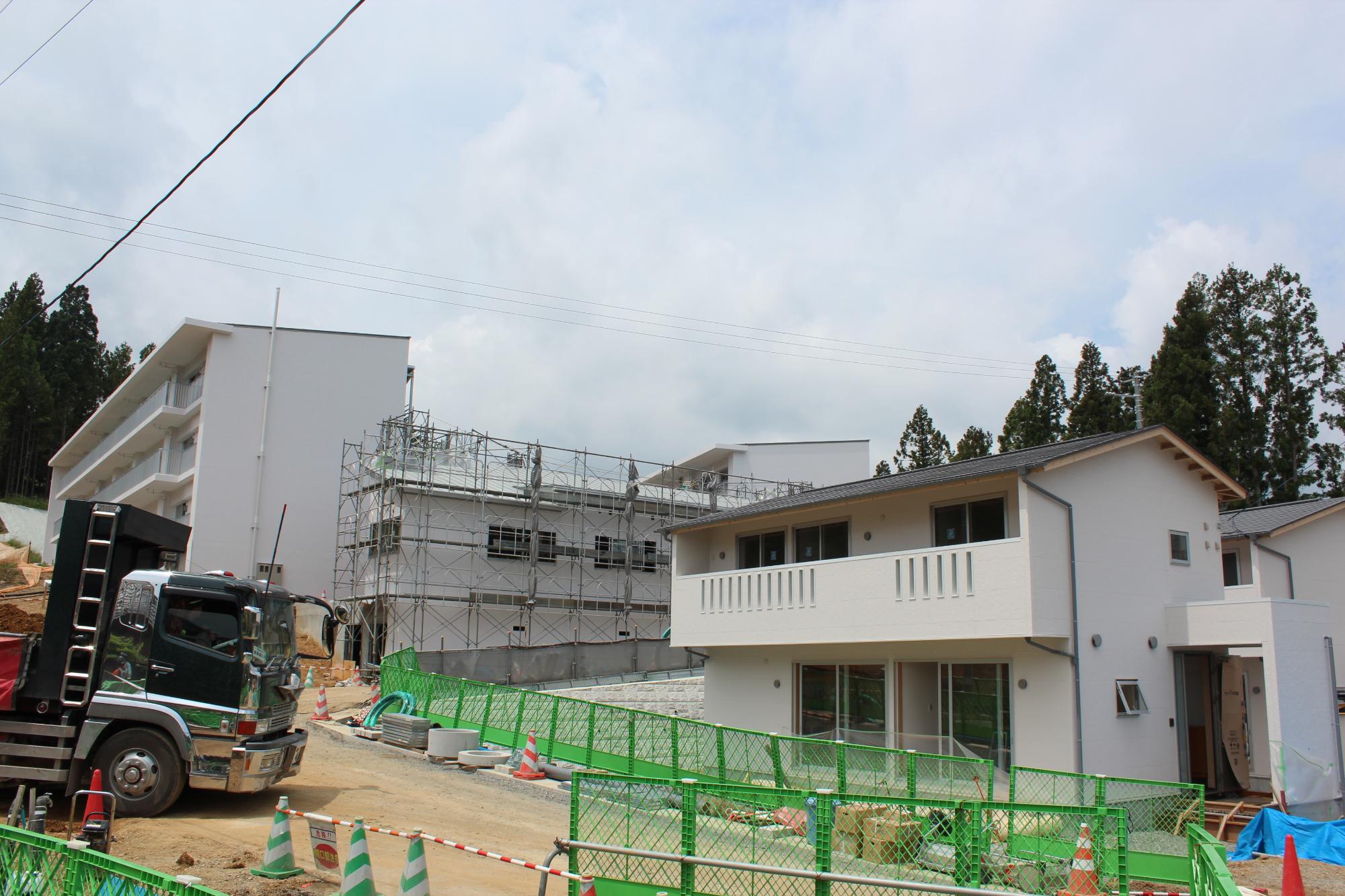 完成した住宅と、背後でまだ足場が組まれ工事が続いている建物が並ぶ住宅地の写真