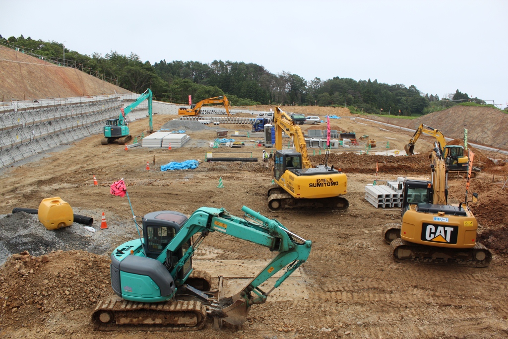 複数の建設機械が密集し、建設資材が積まれている造成工事の真っ最中の写真