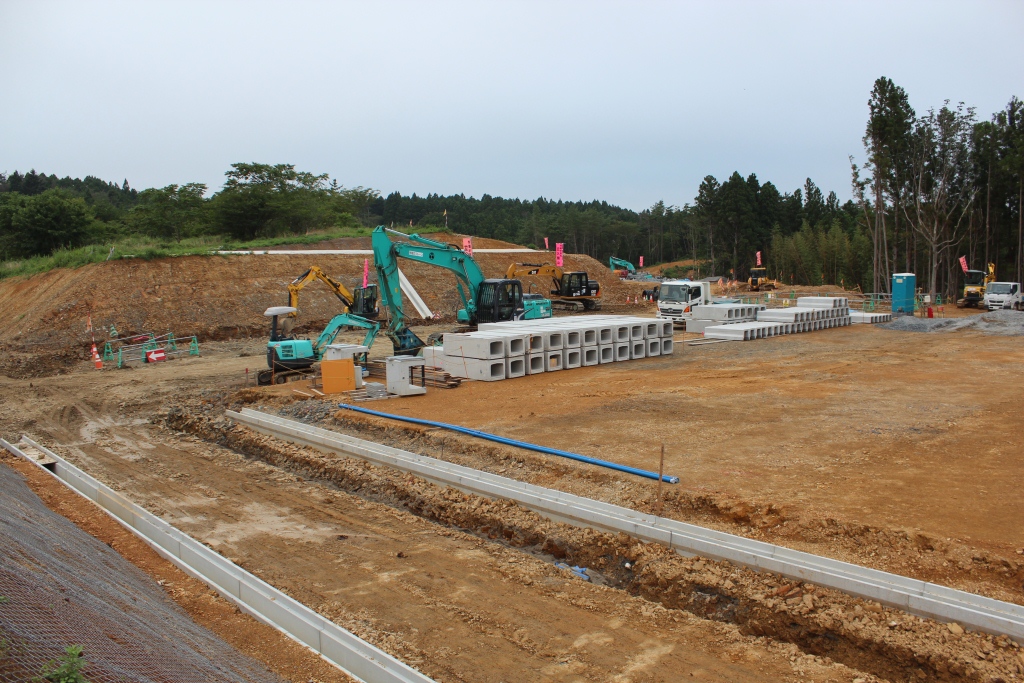 整然と積まれたコンクリート資材と重機が並ぶ造成地の工事中の様子の写真