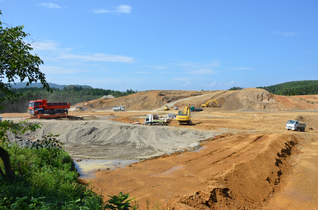 広大な造成地に複数のトラックとショベルカーが土砂や砂利を運び造成工事を行っている写真