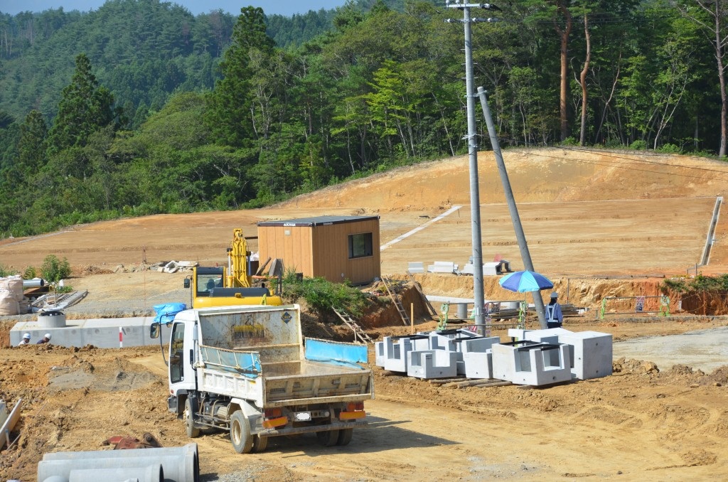 重機やトラックが入り、仮設の建物や資材が集められた造成工事の途中段階の現場の写真