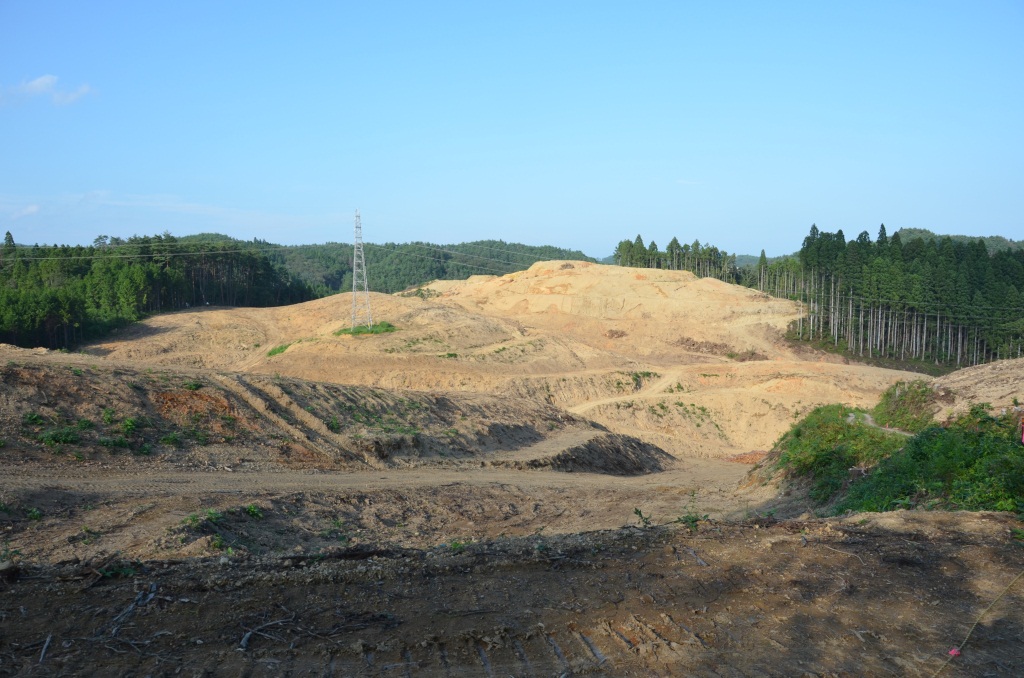 木が伐採され切り開かれた造成地の中央に送電線の鉄塔が立っている写真
