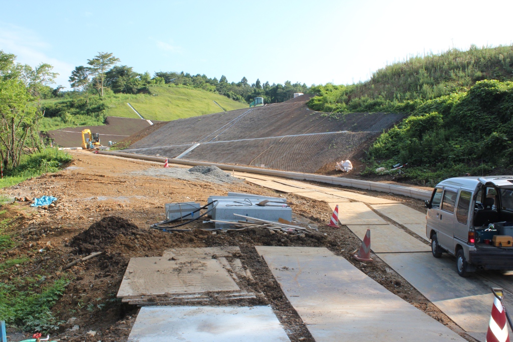 傾斜地にコンクリートの排水路が設置され、重機と車両が工事作業を行っている様子を写した写真