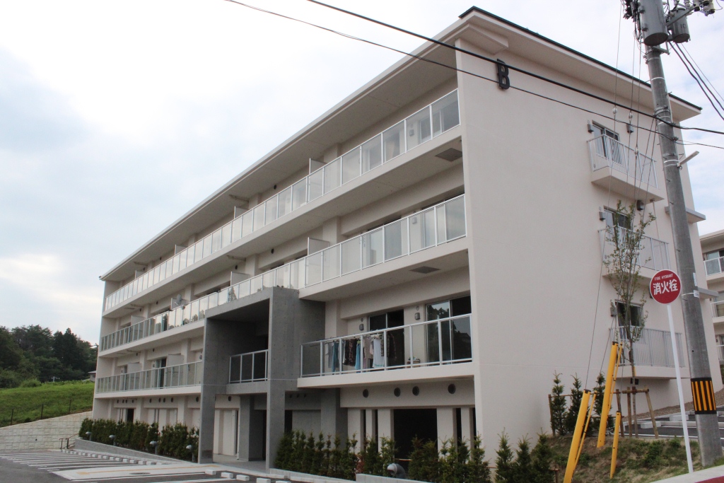 白い外壁とバルコニー付きの3階建て集合住宅の正面を斜め下から見上げた災害公営住宅の写真