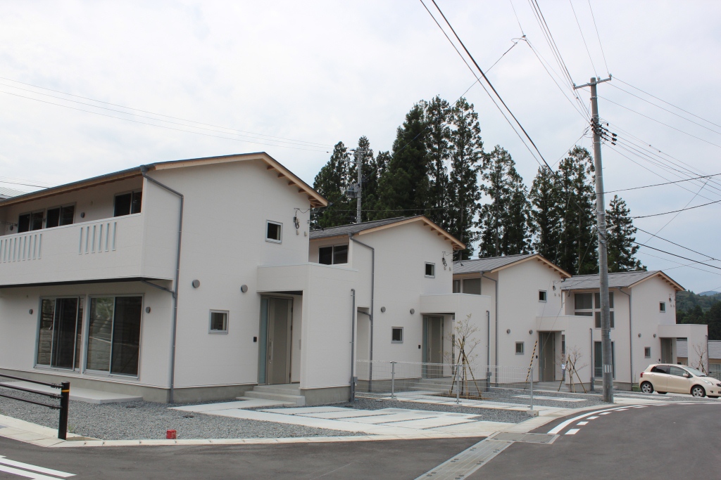 緩やかな傾斜地に整備された道路があり、新しく建てられた駐車場付きの白い一戸建て住宅が4軒並んでいる住宅地の写真