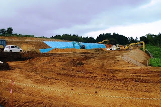 奥はブルーシートがかぶされた建設予定地を写した写真