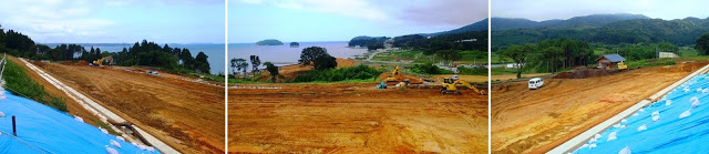 奥に海が広がり、右手には山々、手前の平地には重機がはいり法面にブルーシートでをかぶせている工事現場のパノラマ写真