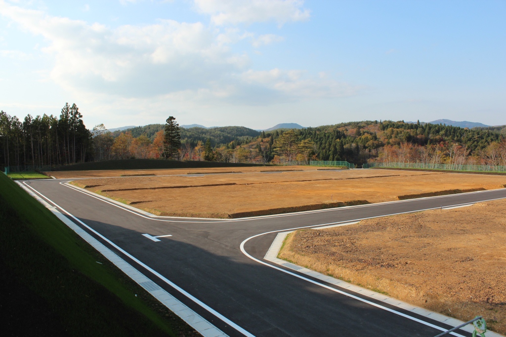 秋の風景の中、舗装された道路と整然と区画された宅地が広がる完成後の造成地の写真