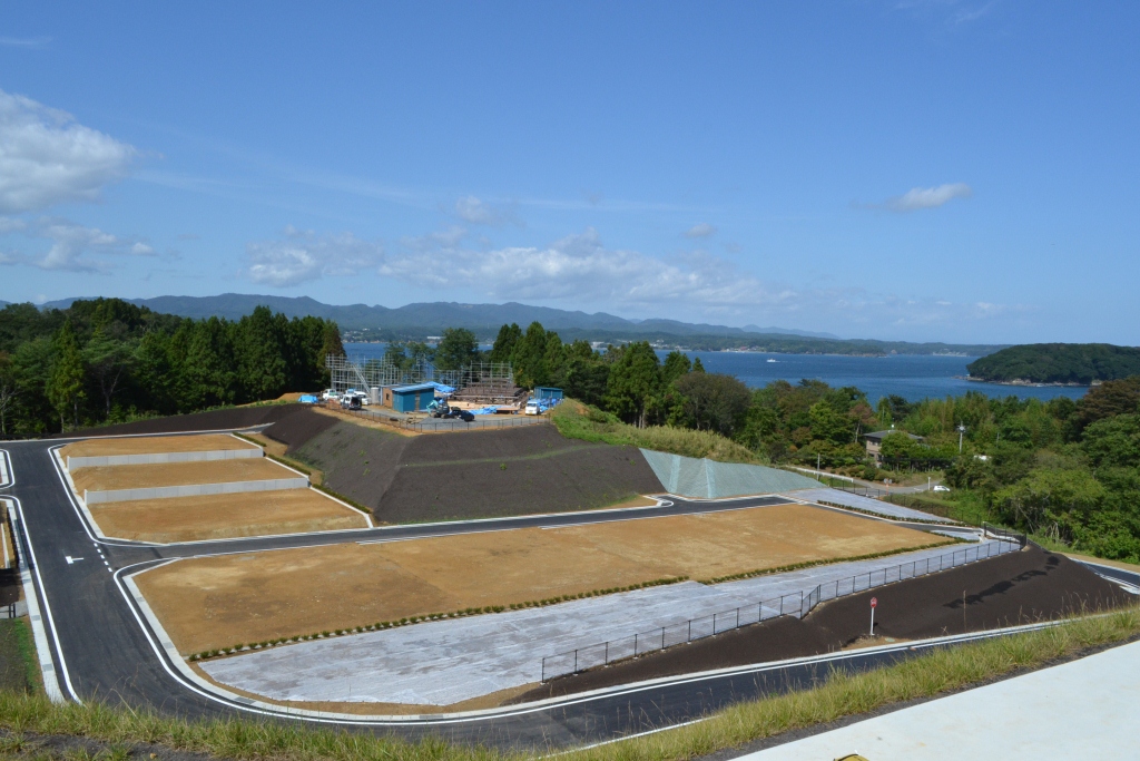 整地と舗装が完了し、住宅地として整った区画と、その背後に広がる海と山並みが見える写真