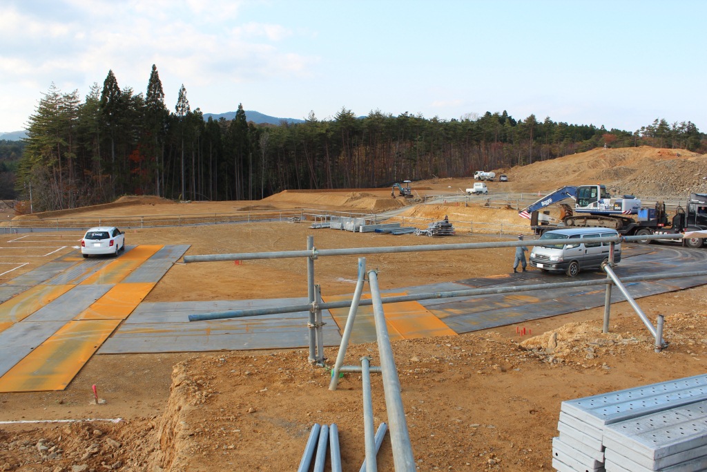 坂の上で複数のショベルカーとダンプカーが土を動かしている工事現場の様子の写真