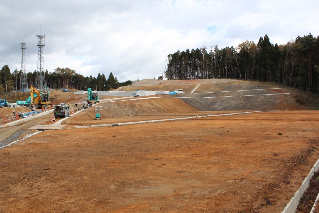 傾斜地に沿って進められる造成工事で、重機や舗装された道、作業中の様子が確認できる写真