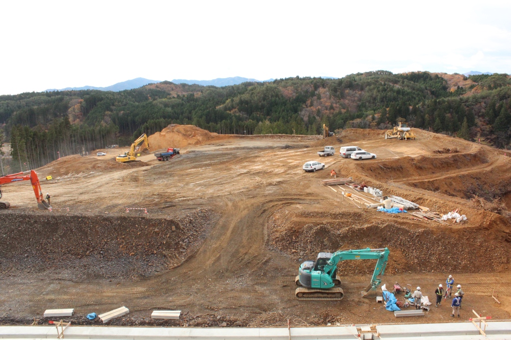 切り開かれた山の上に重機や作業車、作業員が集まり、造成が進められている広い工事現場の写真