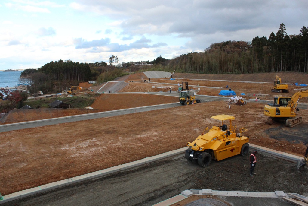 海の近くで重機や作業員が整備された区画を造成している様子の写真