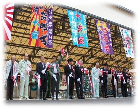 仮設魚市場オープンにて、大漁旗が数枚掲げられ、関係者の方々がテープカットをしている写真