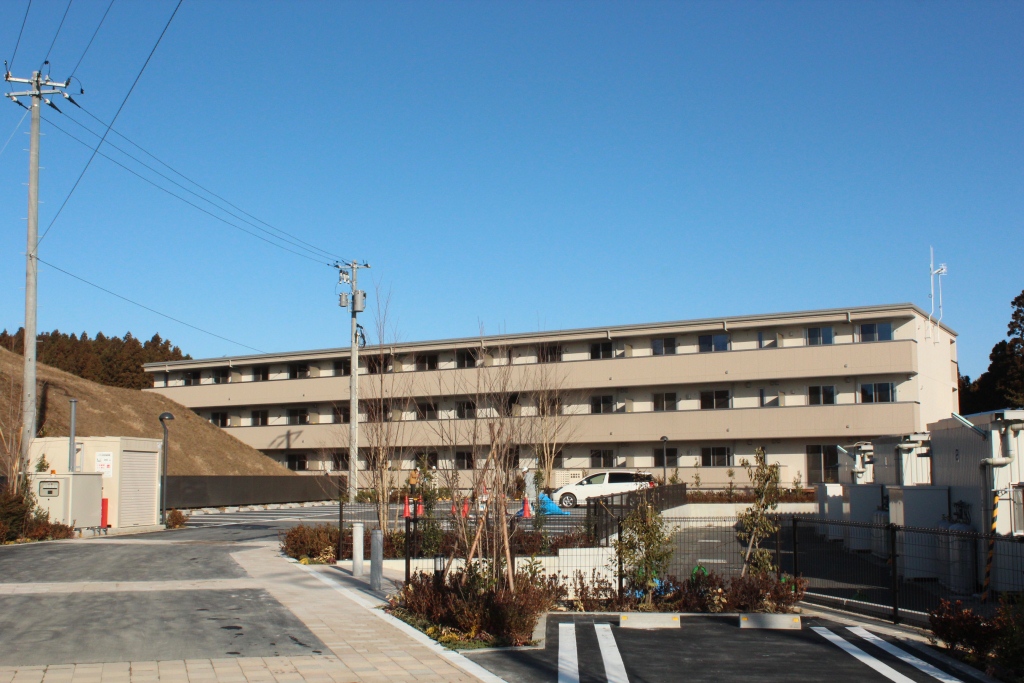 外構や植栽も整備され、駐車場とともに完成した三階建て集合住宅の全景写真