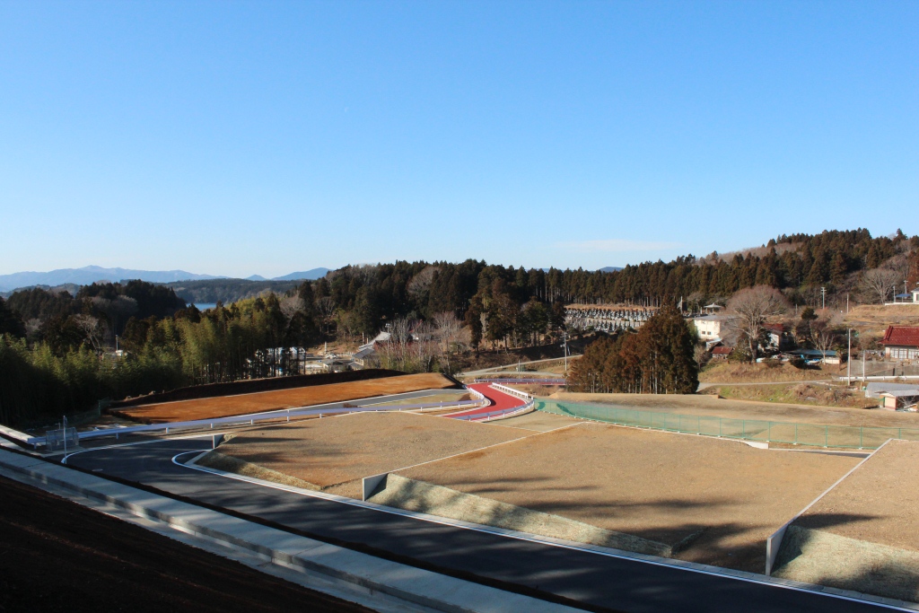遠くに山や湖を望む高台から撮影された、整備された区画と赤い舗装の通路が見える完成した宅地造成地の写真