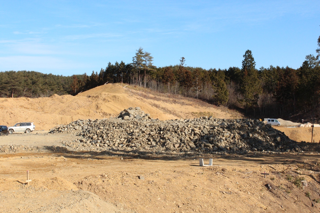 砂利と土が盛られた場所に白い車が複数停まっている造成中の現場の写真