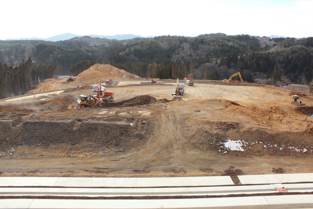山を切り開いた広い土地に大型重機が複数入り、重機や作業車が稼働する土木造成現場の写真
