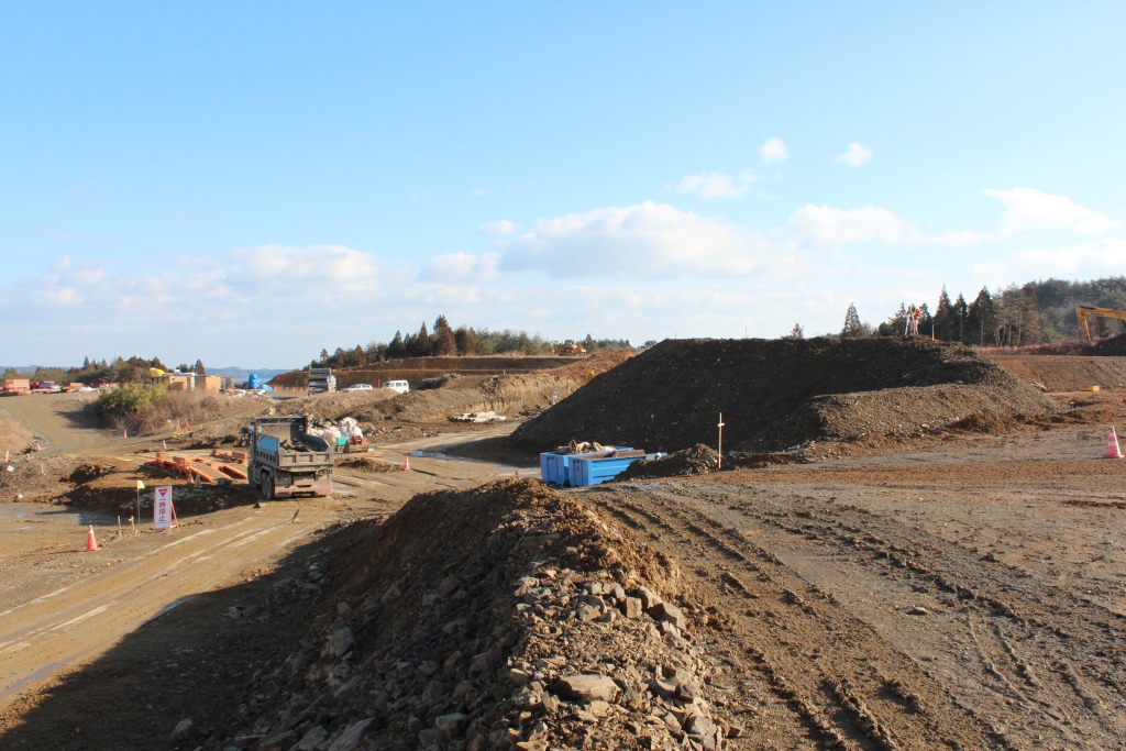 青空の下、大型の重機やトラックが動いている広い造成工事現場の様子を写した写真