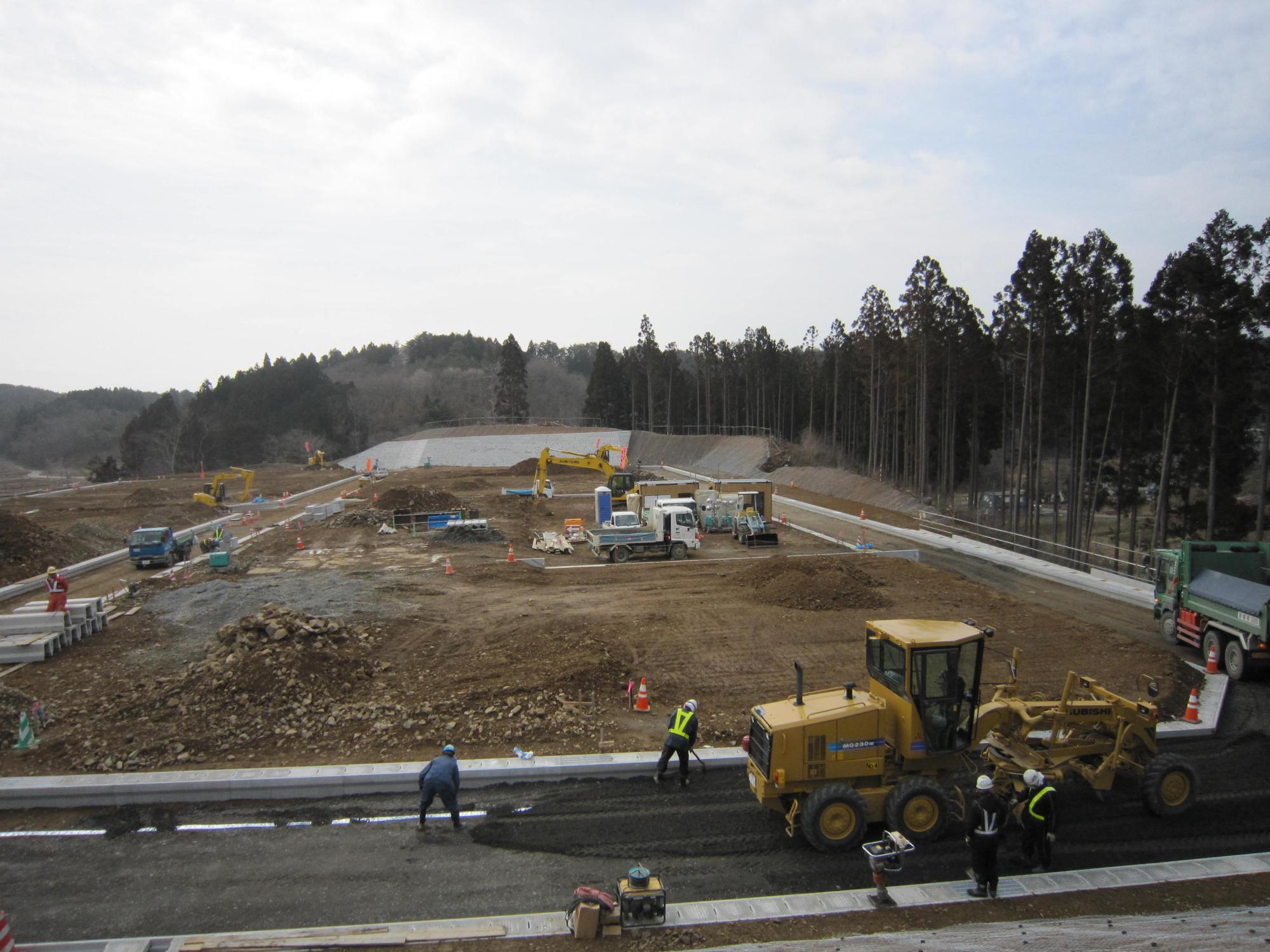 複数の作業員と車両が入り舗装作業が始まった森林の中の宅地造成現場の写真