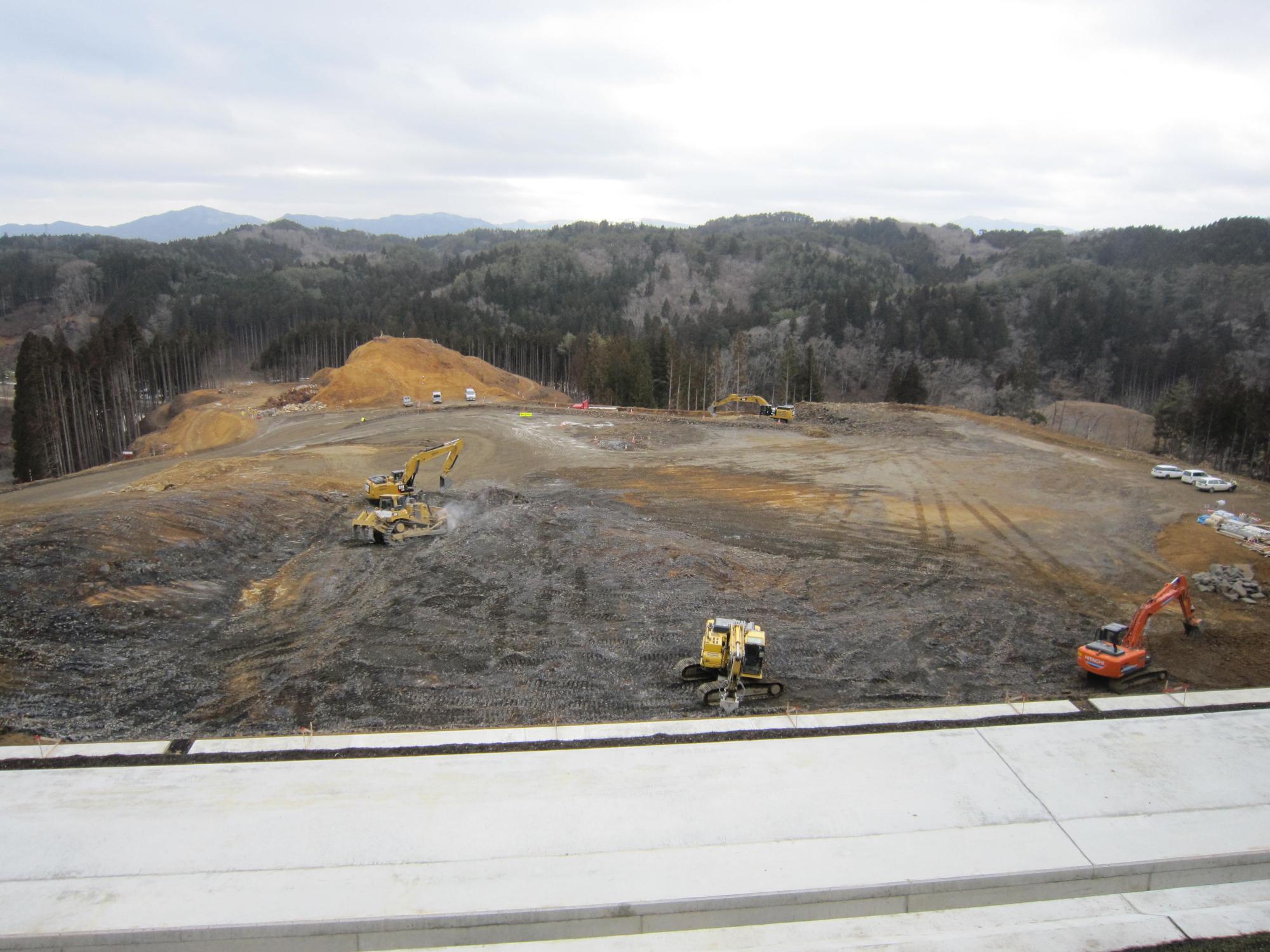山を削って整地された造成地の地面が平らに均され、重機が広範囲に点在している開発工事中の写真