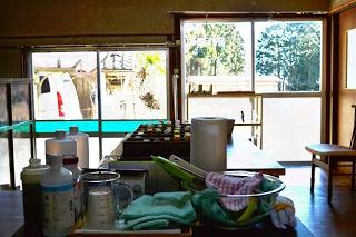 室内のテーブルにはいろいろな道具が置かれ奥のドアから外の風景が見れる工房の写真