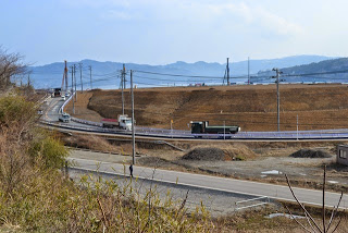 道路が画面を横切るように通って道路上にはトラックや乗用車など複数の車両が走行している写真