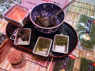 丸いお盆に丸いお椀が置かれ、手前に3個のメカブの試食品が並べられている写真