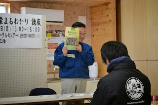 資料を顔の横に持ち上げ説明をしている男性の写真