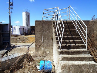コンクリート製の古い階段があり、上には白い鉄柵がついている階段の向こうには白いタンクが立っている写真