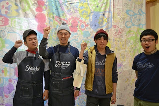 男性3名が右手を曲げこぶしを上にあげたポーズをとり、その隣で男性1人が大きく口を開け記念撮影をしている写真