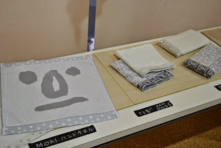 机の上に顔が描かれたタオルとたたまれた布製品が展示されている写真