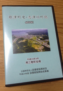 中央に町の航空写真が印刷され「歌津町史・志津川町誌 e-BOOK」とタイトルが書かれたDVDケースが机の上に置かれている写真