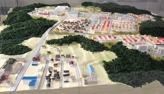 山に囲まれた中に赤や青、黒の屋根がついた建物が並んだ住宅地などが整然と配置されたジオラマ模型で、開発後の街の様子を再現している写真