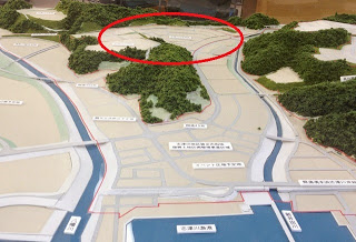 2本の川や道路に囲まれた市街地模型の写真の一部に赤い丸が描かれ、特定の開発予定区域が強調されている画像