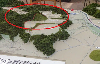 ジオラマの写真の山に囲まれた谷あいの土地を赤丸で囲んで示し、そこが新たに開発される予定地であることを示している画像