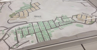 白い地形模型の上に淡い緑色の建物群とベージュ色の住宅地が区画ごとに配置され、中央を貫く道路が街の構造を示している模型の写真