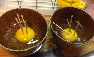 木製の器の中に卵がそれぞれ浮かんでおり、右側に入っている卵に刺さった爪楊枝は倒れたりしているが、左側の自然卵に刺さっている爪楊枝は4本とも真っすぐ立っている、弾力を比較している写真
