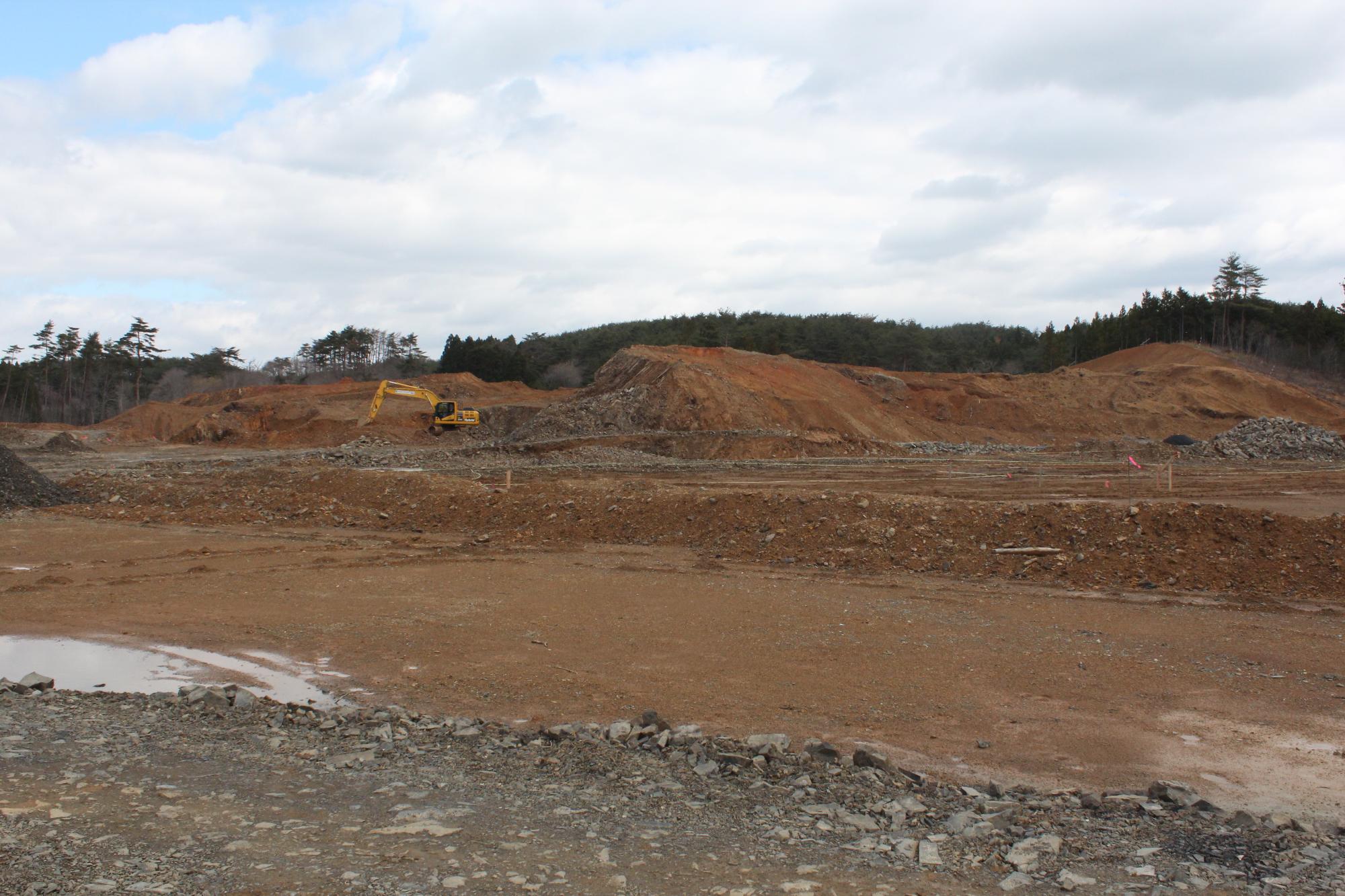 重機が土を掘り起こしながら整地が進んでいる赤茶けた造成地の写真