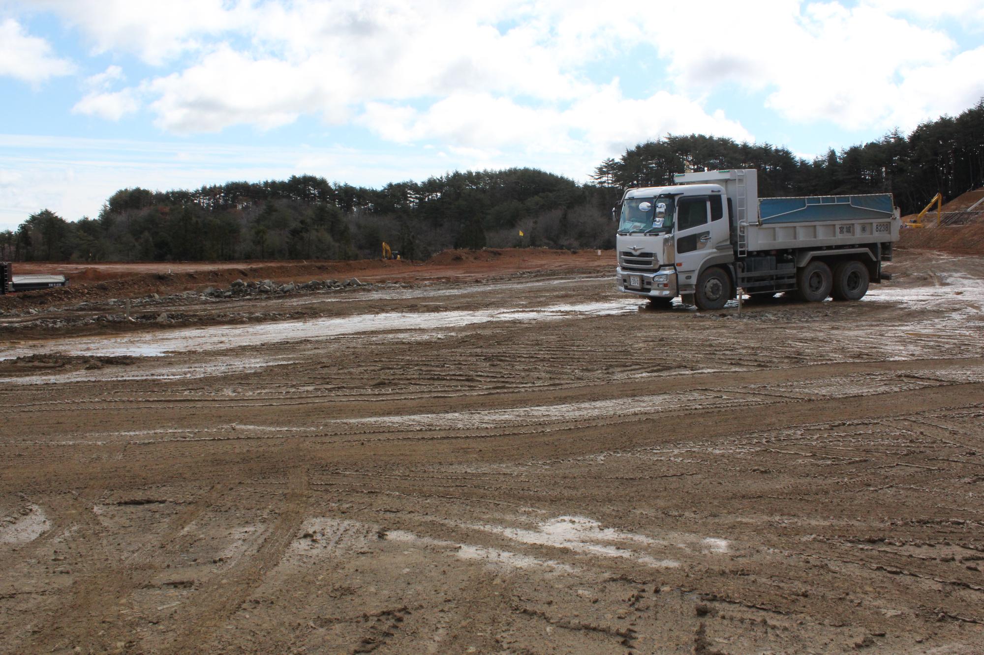 ぬかるんだ広い工事現場に大型のダンプカーが1台ある写真