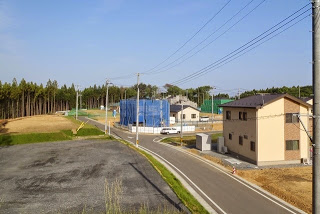 新しい舗装道路の先に複数の建設中の住宅や、新築住宅が建ち並び、電線が張り巡らされた郊外の新興住宅地の写真