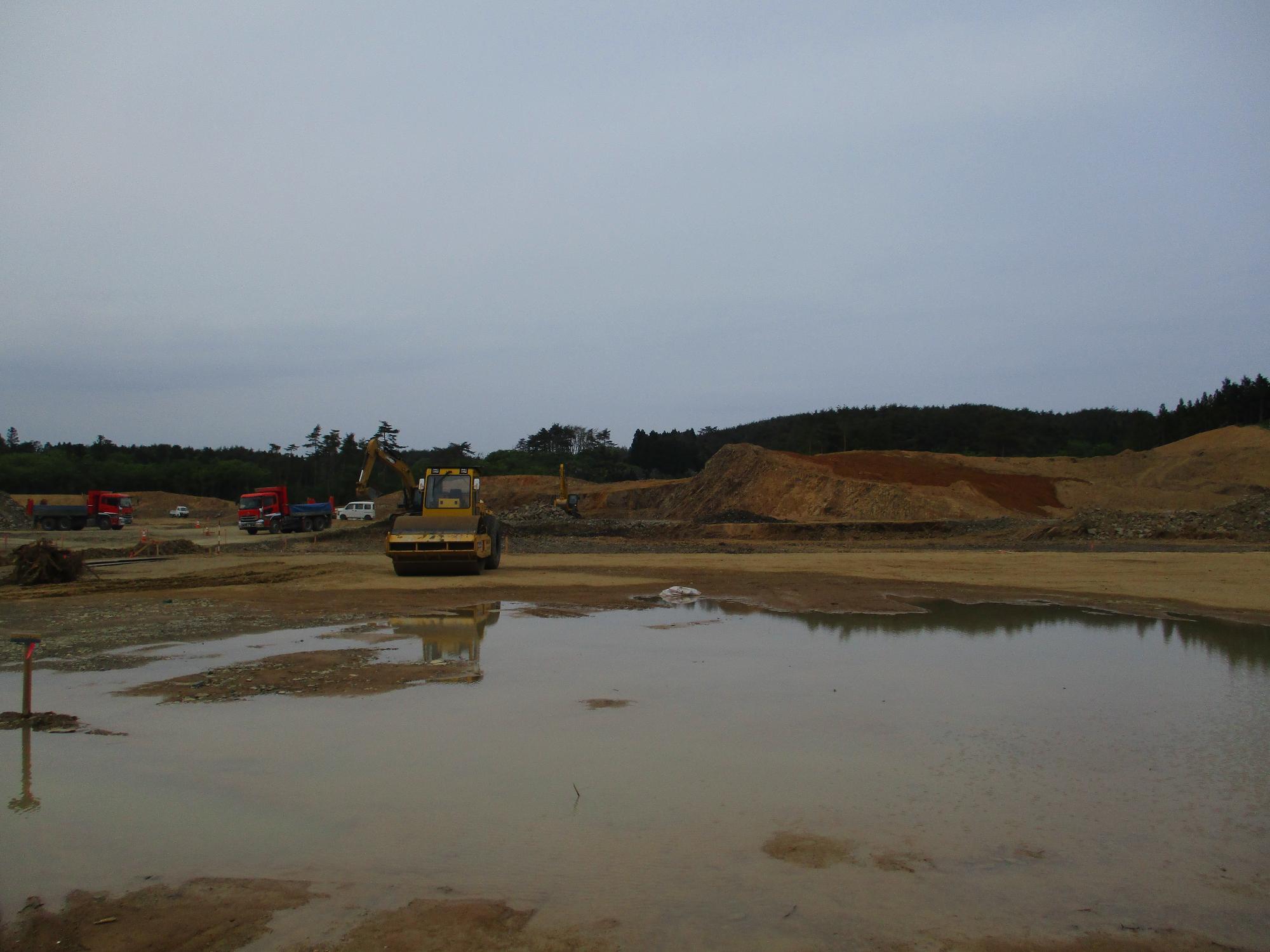 大きな水たまりの前にローラー車が止まっている工事中の敷地の写真