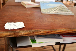 木製の古い机の上に一枚のメモと本が置かれ、引き出しの中には複数の本が収納されている、手作り感のある本の展示風景の写真