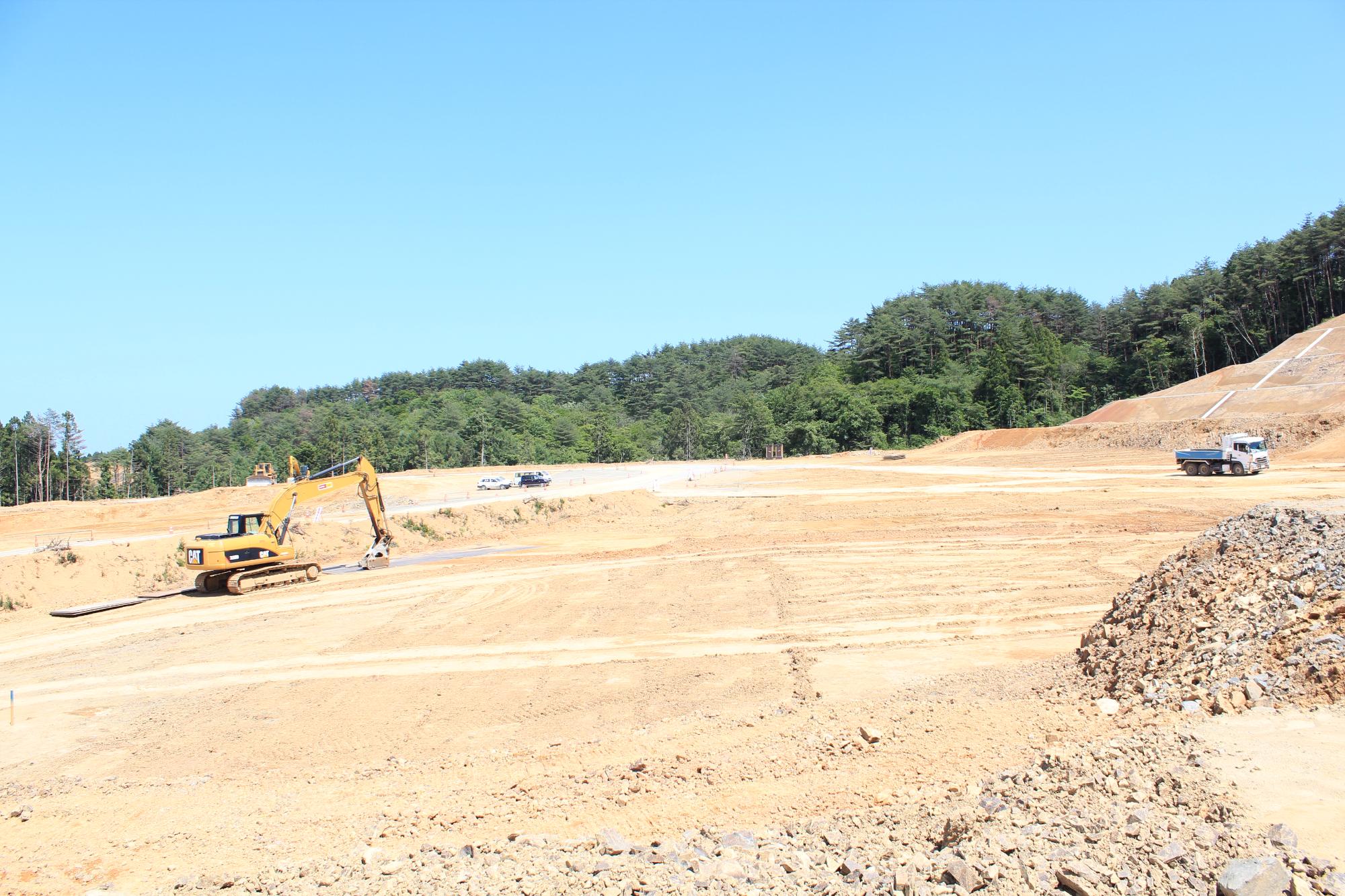 森林の前で重機やダンプトラックが使われ、広い土地の造成工事が行われている写真