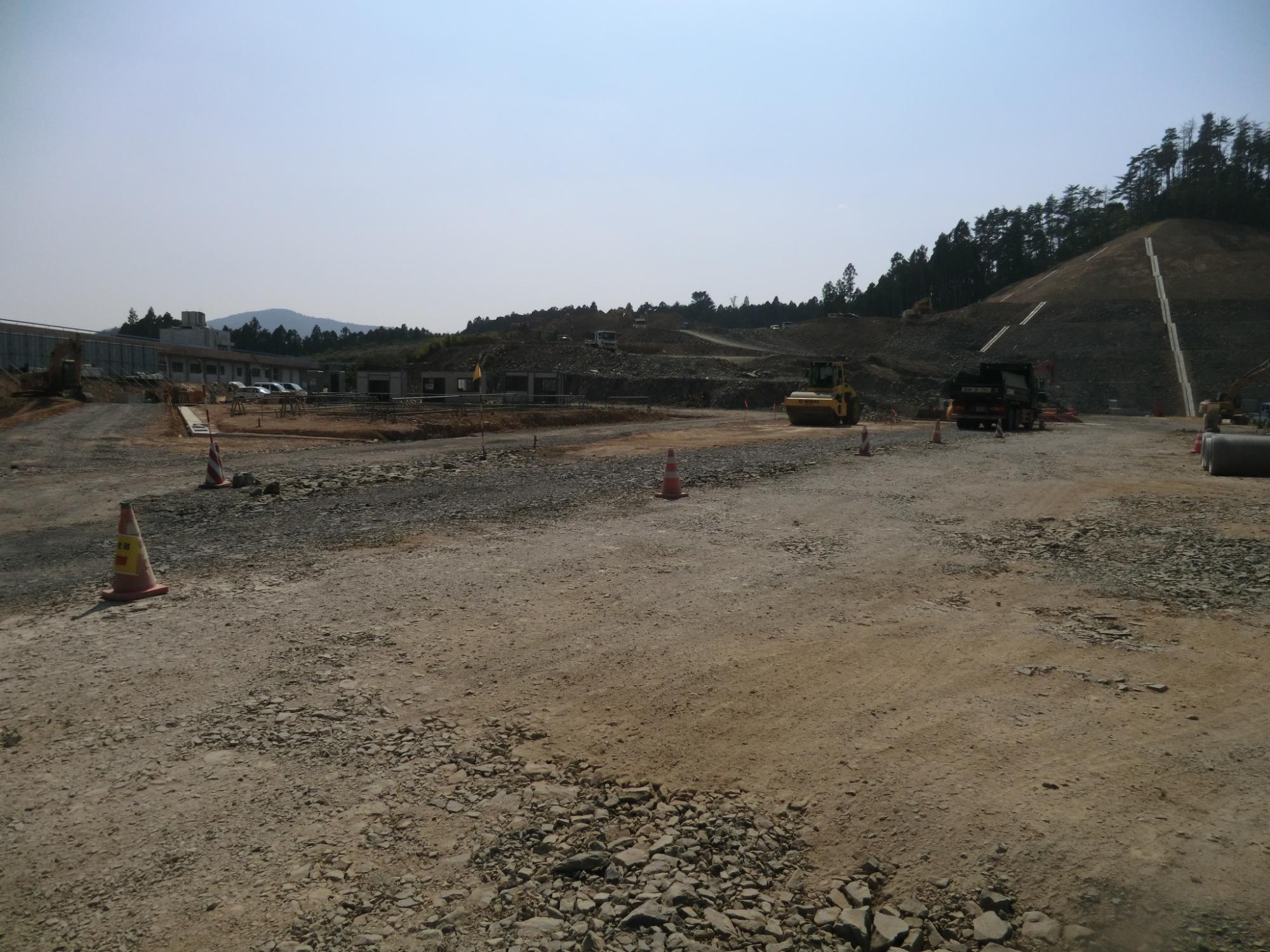 山を背景に地面に等間隔にコーンが並び、重機やトラックが活動している造成地の写真