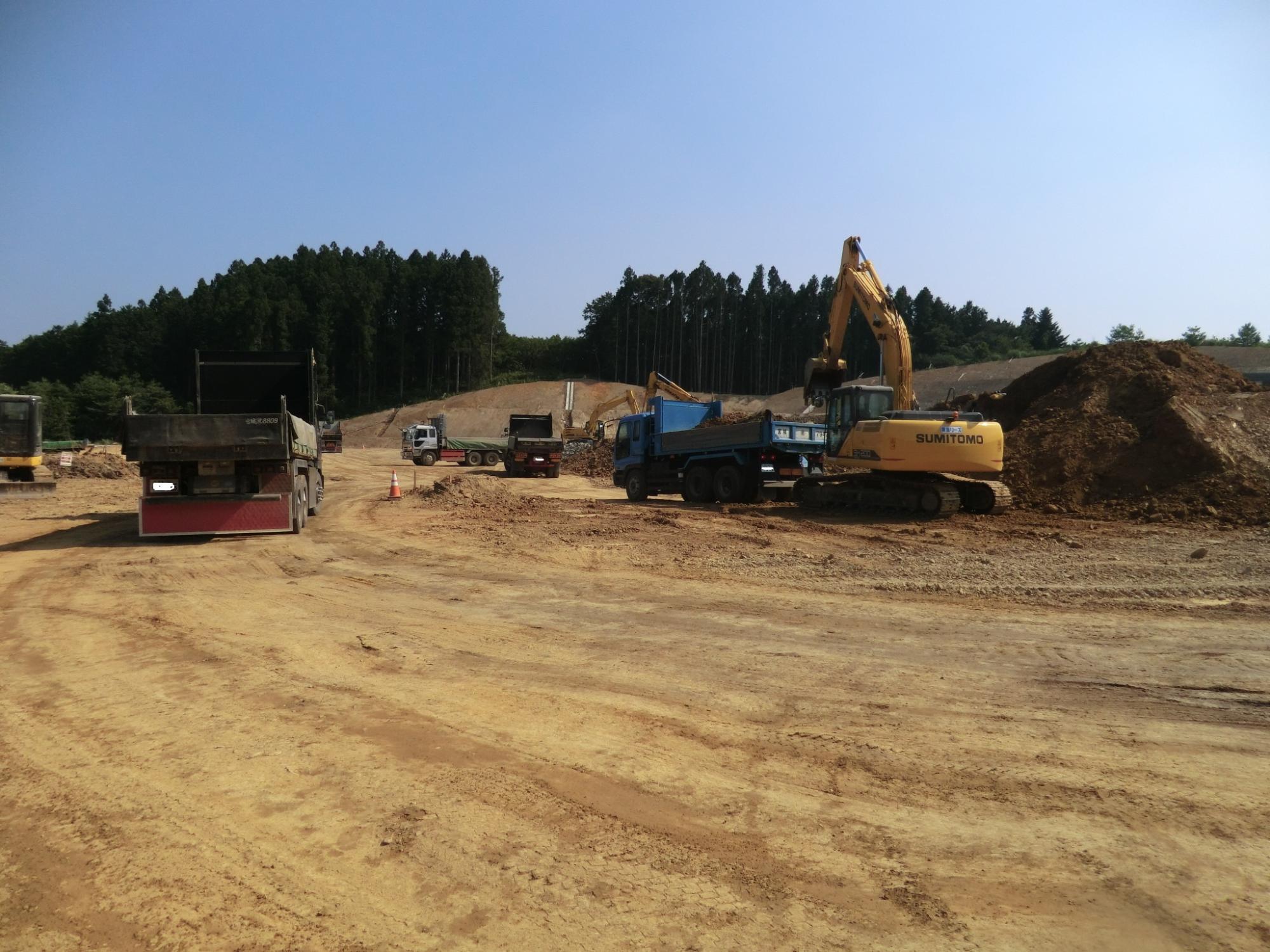 山の土を積んだり運搬したりしている重機やトラックが見える造成現場の写真