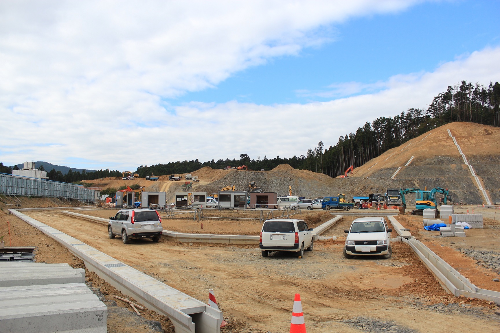 プレハブや資材が並びコンクリートの縁石が設置されている造成現場の写真